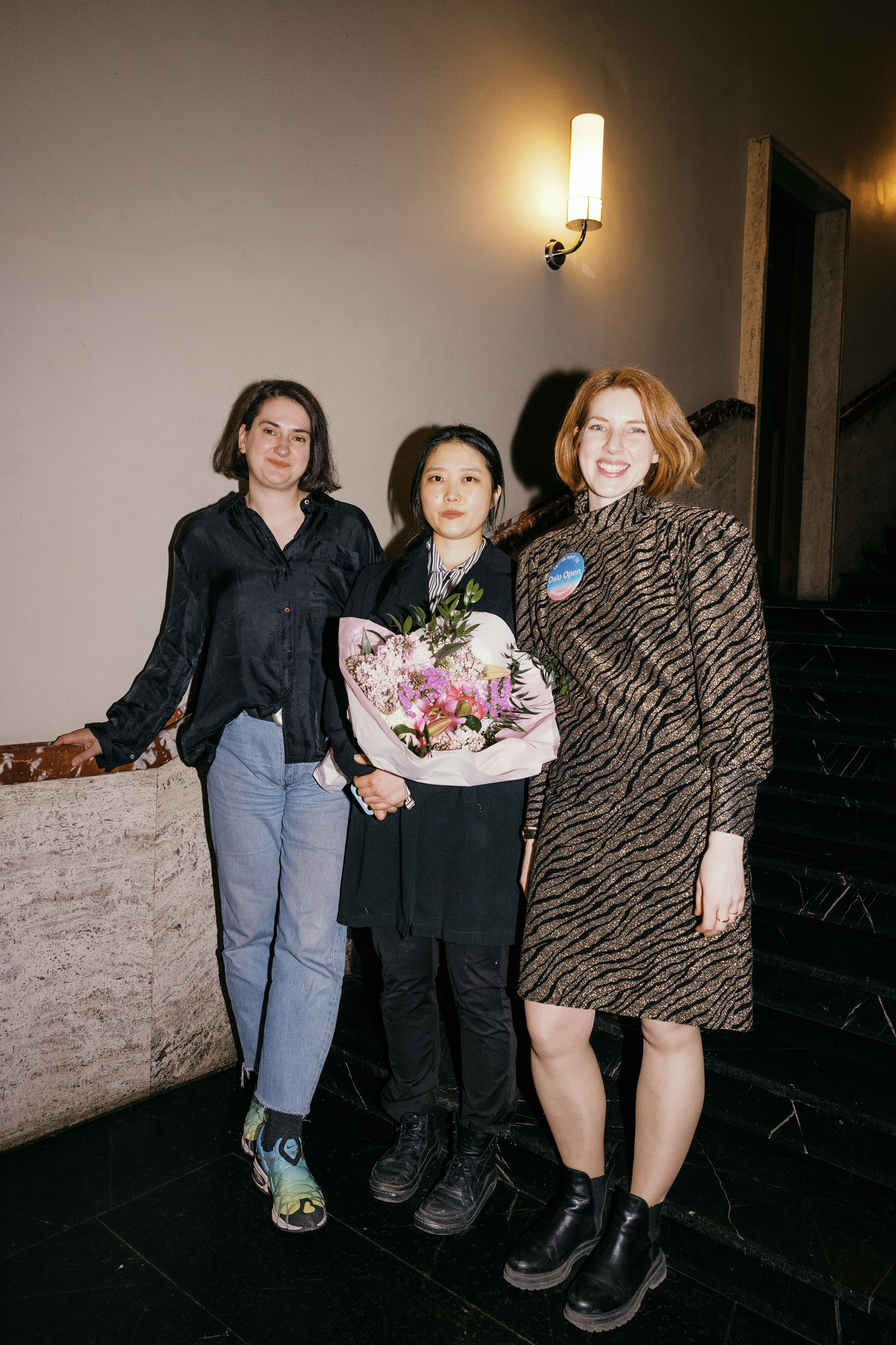 Tre personer står side om side: Jasmina Kemura (kunstfaglig rådgiver i KPA), kunstner Naeun Kang og Frida Rusnak (daglig leder i Oslo Open). Naeun Kang holder en blomsterbukett.