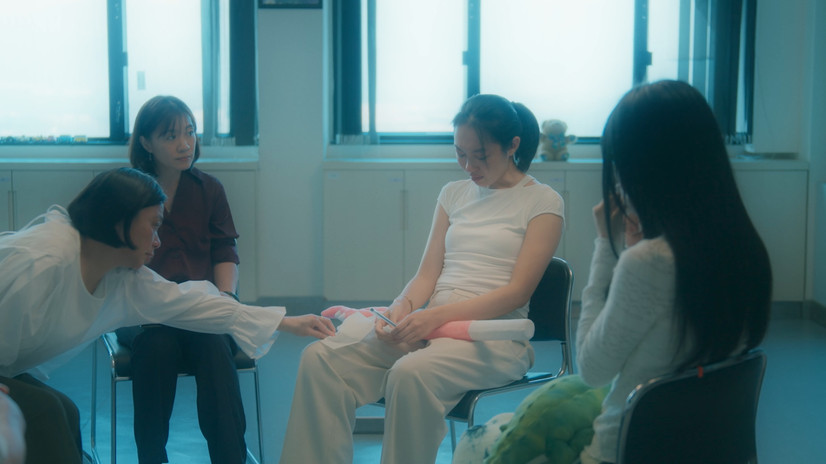Film still from the short film Whispers in the Belly (2025) by Yu Shuk Pui Bobby, showing a Hong Kong family and Ling’s foreign boyfriend in an emotionally charged conversation; the film explores abdominal pain, family secrets and intergenerational conflict through conversational therapy and shifting aspect ratios.