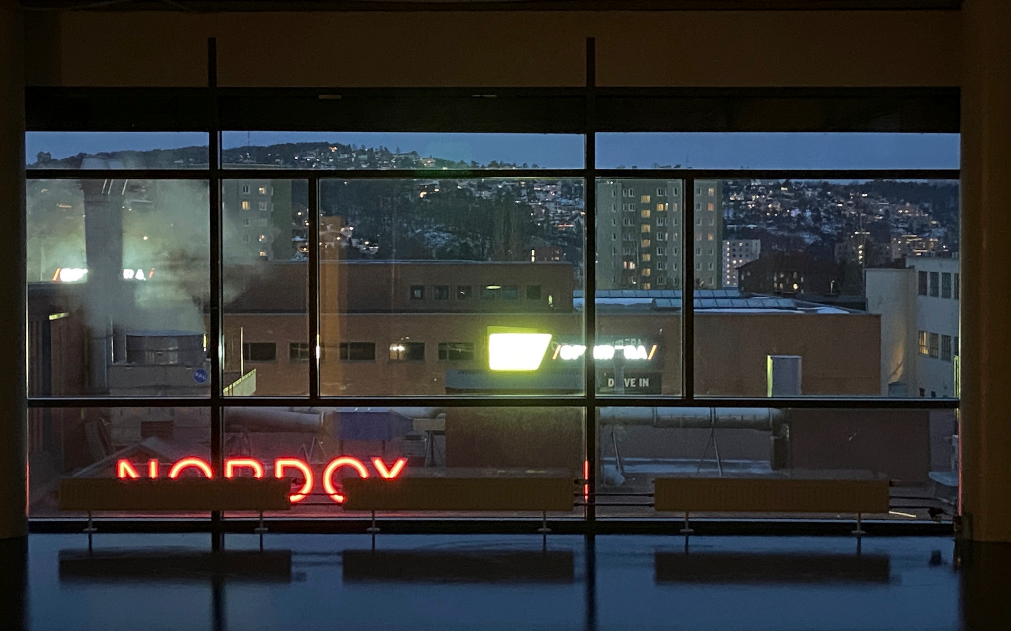 Bymiljø i kveldslys med fjell i bakgrunnen fotografert gjennom et vindu