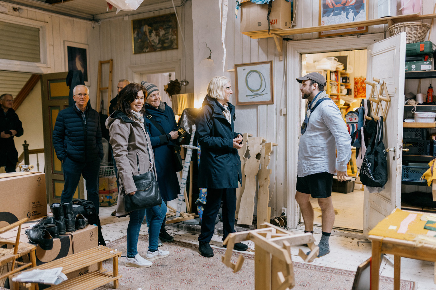 Bilde fra et atelier med masse ting liggende runt om kring, kunstner Fredrik Floen står til høyre ved døråpningen til et annet rom og snakker med en gruppe gjester