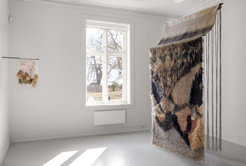 To abstrakte bilder laget med ryeteknikk. En liten på venstre side, øverste del av verke er hvit, ned er det grønn, gul og beige. Montert sidelengs på vegg med den stål stang. En annen stor rye på høyre side. Henger fra taket med to stål stanger. Farge er grønn, gul og beige. Øverste del av verket er en stripete flat vev og former en slags take, lange rennings tråder henger på baksiden. Fremste side har floss. 