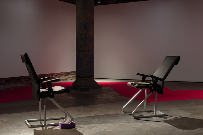 Installation view of Therapy: two black paper chairs face each other with a small paper tissue box, paper pen and paper clipboard between them, suggesting a quiet, miniature therapy room.