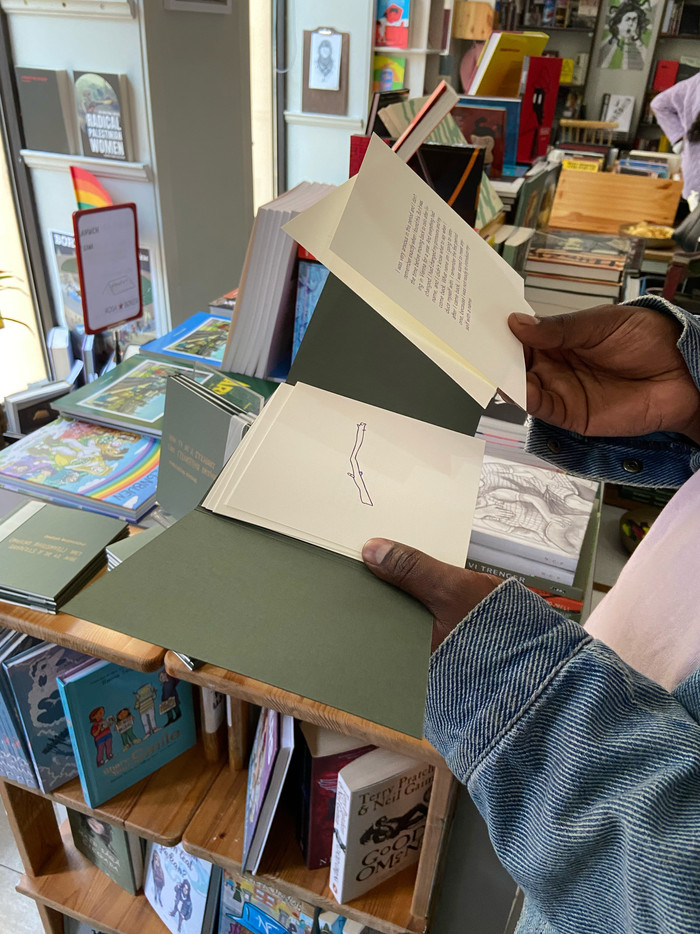 En der holder en åpen publikasjon. Man ser en tegning av en pinne og en bit tekst. 