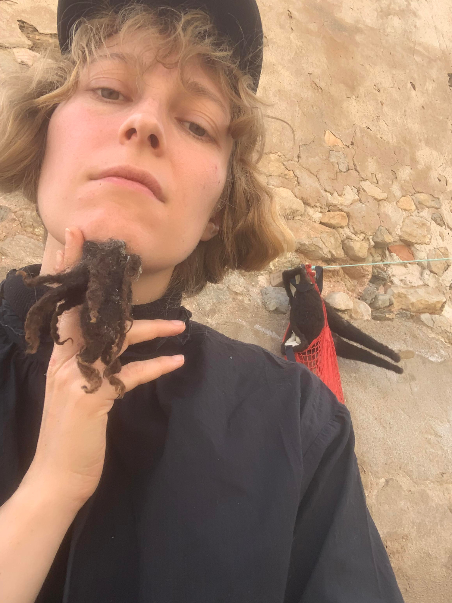 En selfie av kunstneren som holder et løsskjegg foran haka.