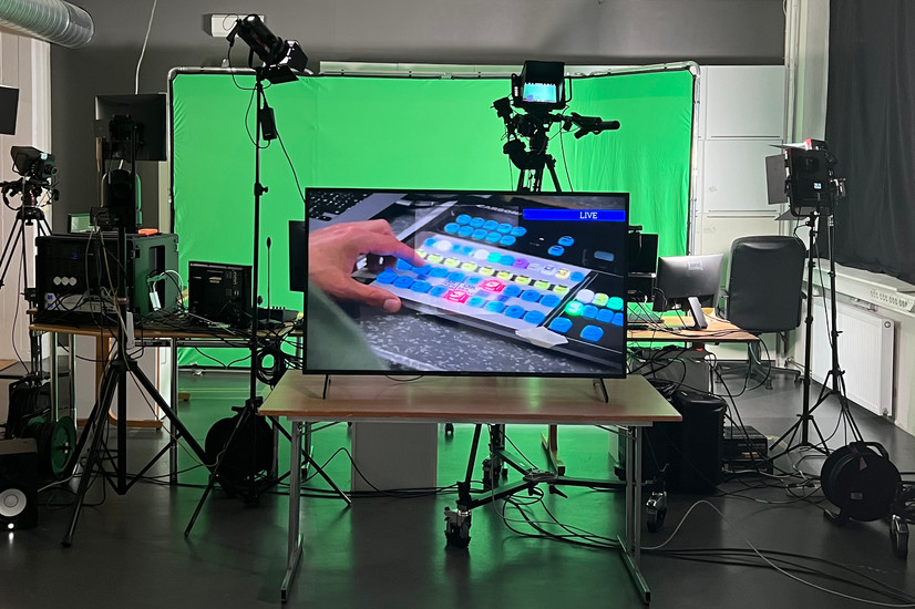 TV-studio med kameraer, lys og greenscreen. Monitor med direktesending av hånd som redigerer.