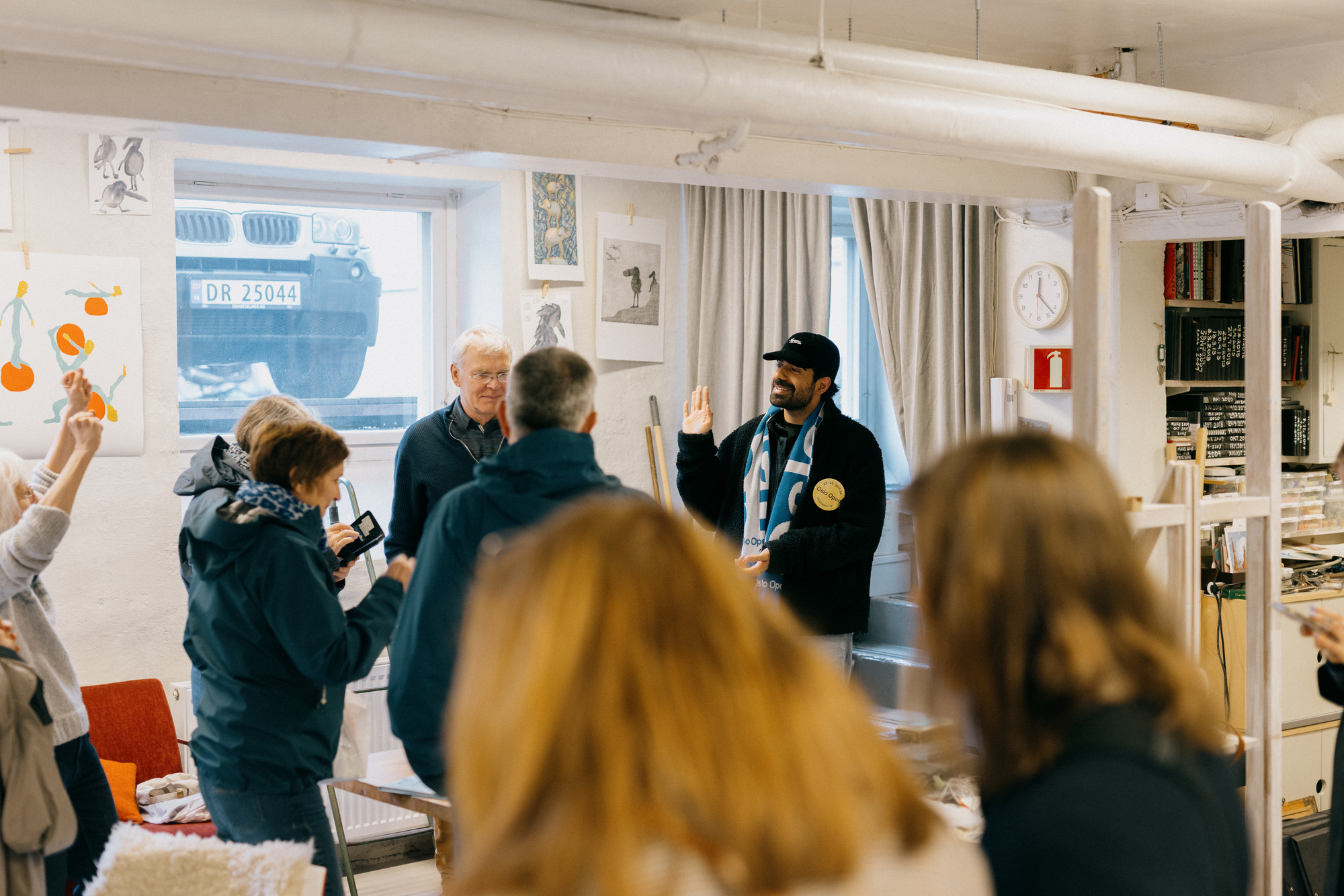 Bilde fra et atelier med en gruppe mennesker vendt mot en smilende ung man med keps og en button der det står Oslo Open.