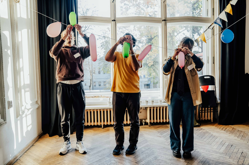 Tre personer setter ballonger fast på en snøre, som en del av en dekorasjon. 