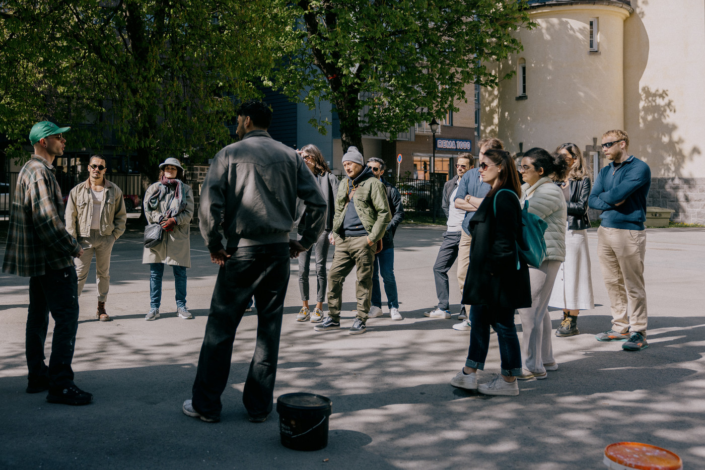 Titalls personer står samlet i ring rundt en person med keps som snakker. Det er en solig vårdag.