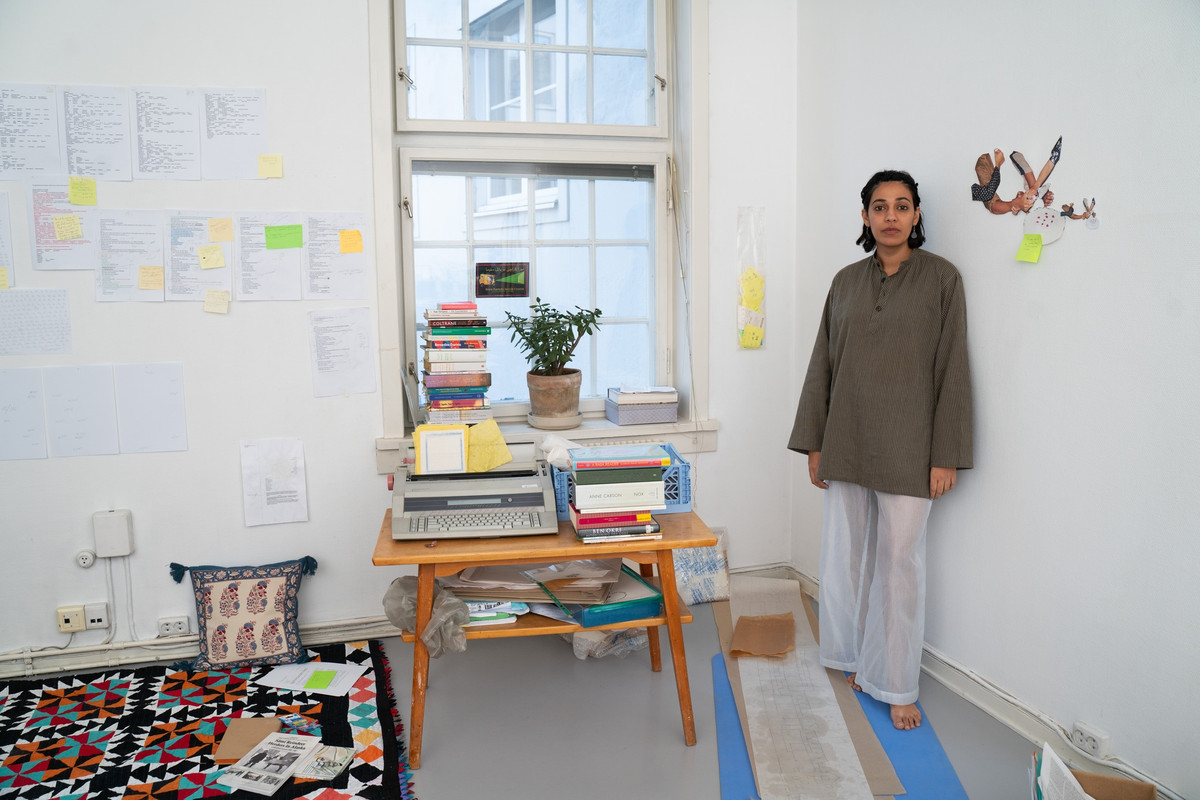 Kunstneren står i et lyst og ryddig atelier, med papirer og gule lapper på veggene.