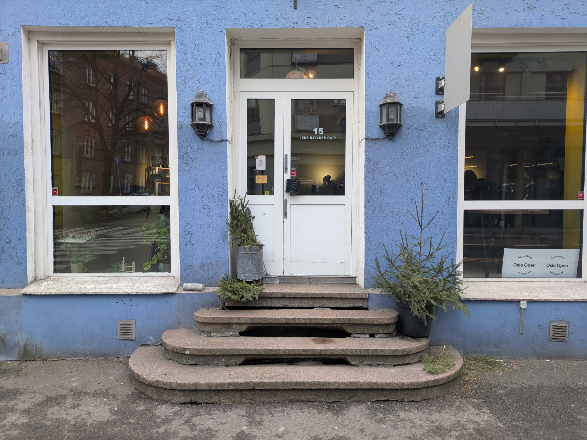 Nærbilde av et hus med blå vegg, i midten en dørr med steintrapp foran og store vinduer på hver side.