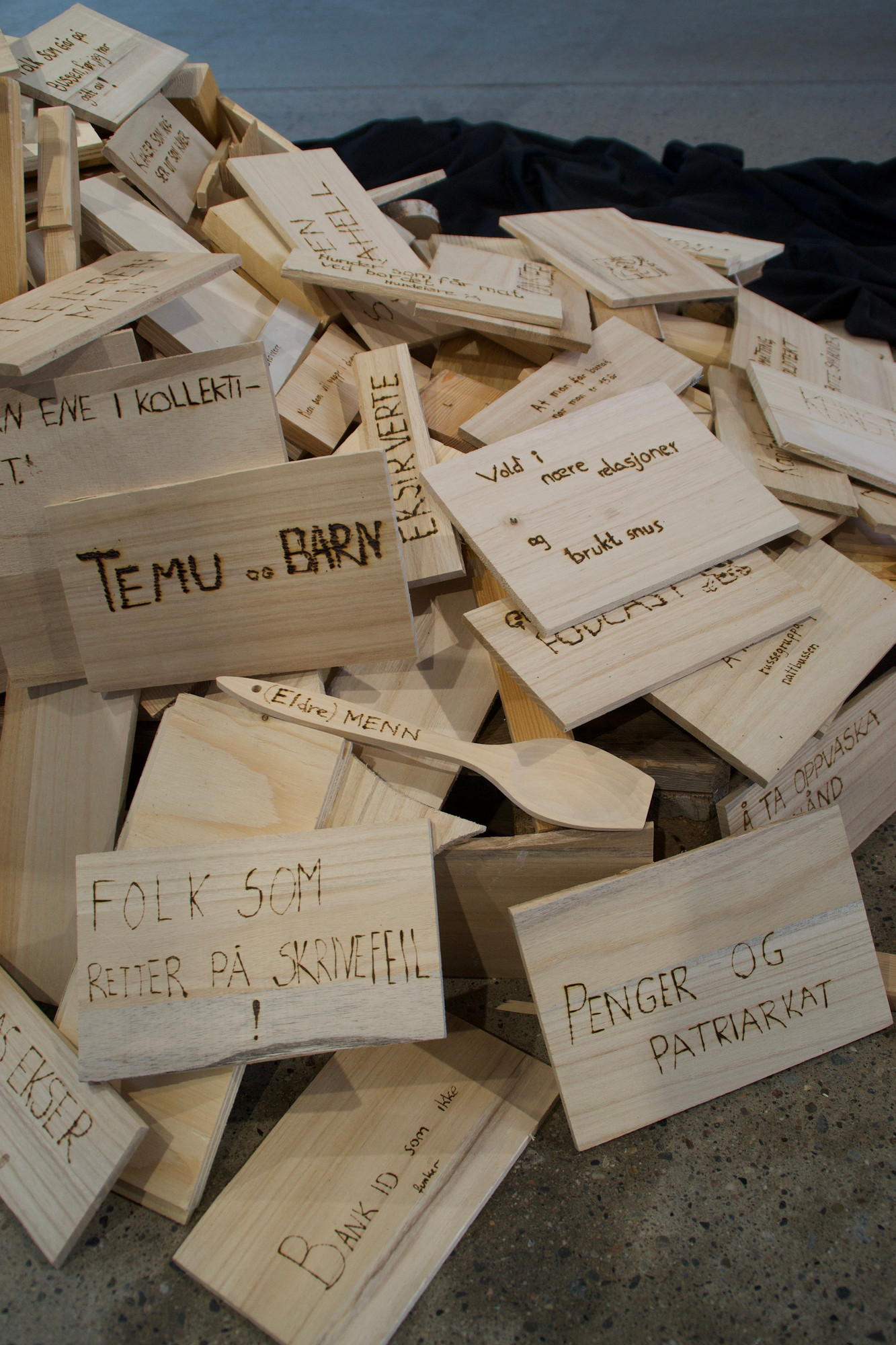 En haug med trebiter med tekst skrevet med svipenn. På trebitene står det for eksempel: Folk som retter på skrivefeil, penger og patriarkat, vold i nære relasjoner og brukte snus