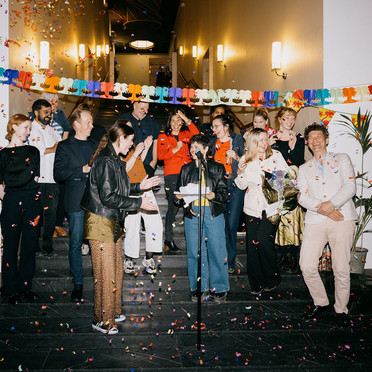 Femten representanter for Atelier Kunstnerforbundet er samlet i trappa på Kunstnernes Hus, omgitt av en sky av konfetti.