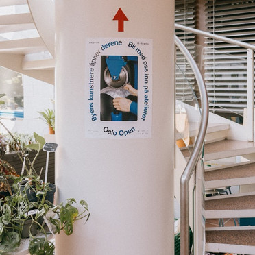 Et bilde av en vindeltrapp. På en søyle henger en plakat fra Oslo Open og en pil peker opp.