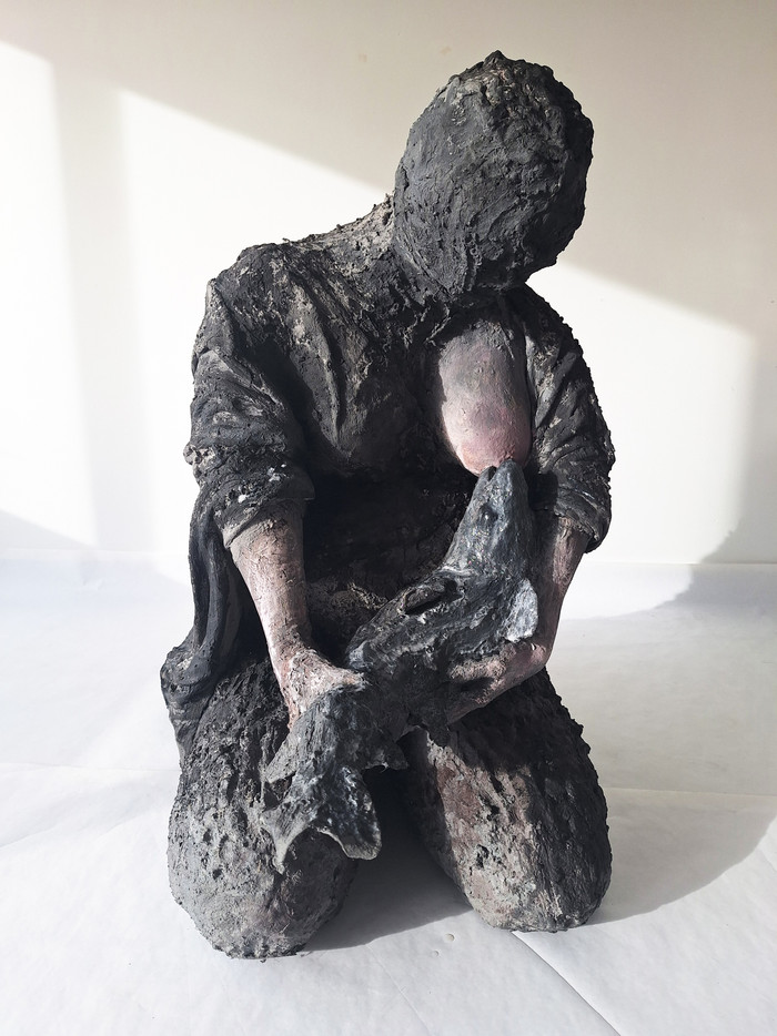 En steinete og sittende kvinnefigur ammer en fisk.